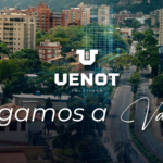 Esta es una imagen a vista de pájaro de la ciudad de Valera, en el estado Trujillo de Venezuela. Se aprecian numerosas casas de techos rojos en primer plano, seguidas por una franja de vegetación y una avenida principal que atraviesa la ciudad. Al fondo, se elevan imponentes montañas verdes que enmarcan la escena urbana. La imagen destaca el desarrollo de la ciudad en medio de un entorno natural montañoso. El cielo está nublado.
